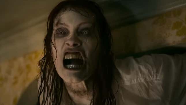 A screenshot of a creepy zombie deadite woman with pale skin baring her teeth at the camera, from Evil Dead Rise