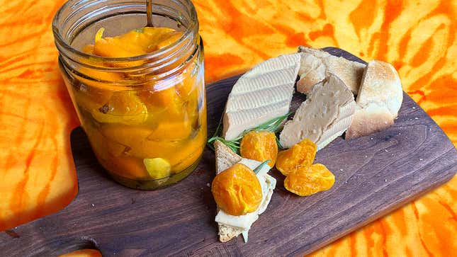 Jar of preserved clementines on wooden cutting board with brie and sliced bread
