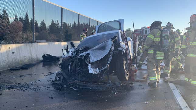 Firefighters stand next to a Tesla Model S destroyed by a battery fire.
