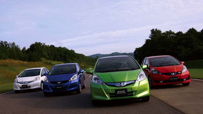 A photo of white, blue, green and red Honda Fit cars driving down a road. 