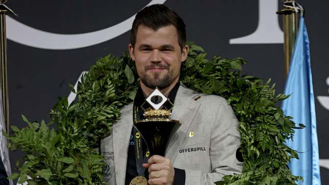 Chess World Champion Magnus Carlsen holds a trophy and smiles. 