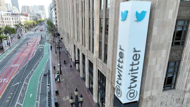 A sign outside a big concrete building of Twitter headquarters reads @twitter with the blue twitter bird above it.