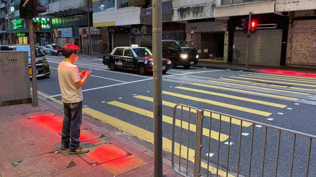 A pedestrian bathed in red light waits for a walk signal at a crosswalk.