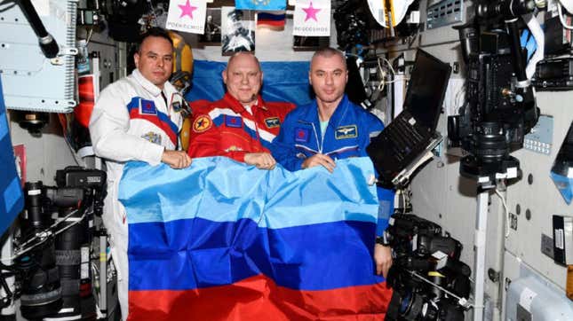 The three astronauts holding up the flag of the Luhansk People’s Republic and the Donetsk People’s Republic.