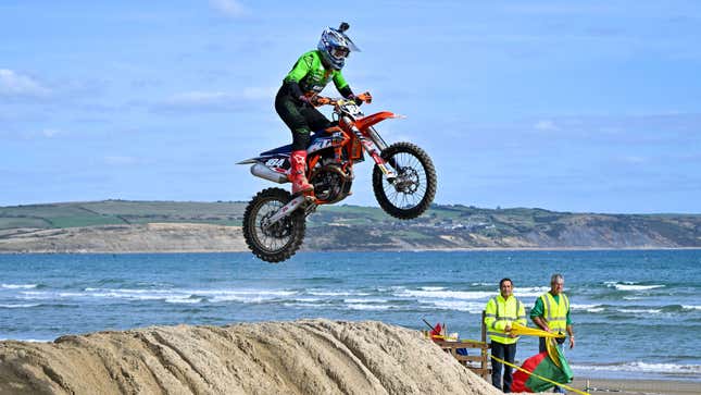 A photo of a dirt bike rider making a jump on a beach in the UK. 