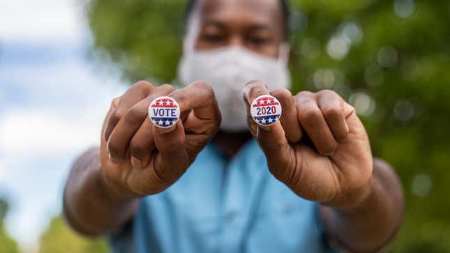 A man holds up two small pins reading "Vote 2020"