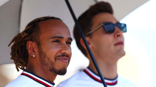 A photo of Lewis Hamilton and George Russell sheltering from the sun under an umbrella.