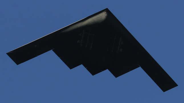 A stealth bomber shot in silhouette against a blue sky.
