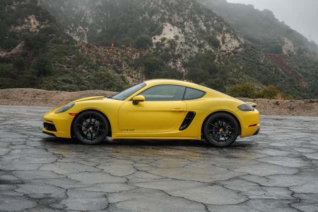 A 2022 Porsche Cayman GTS 4.0 in side profile on wet pavement.