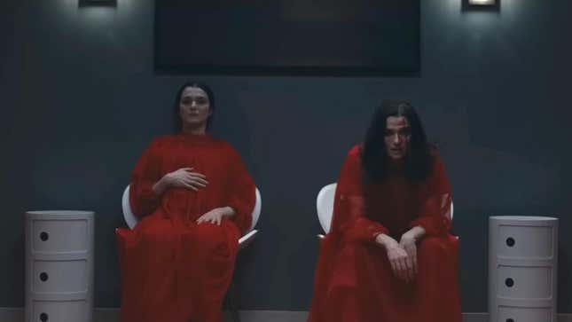 Two women in red hospital gowns, one of them pregnant, both played by Rachel Weisz, sit in waiting room chairs looking exhausted 