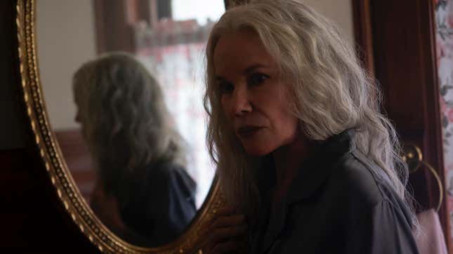 Barbara Hershey, with long grey hair, stands reflected in a mirror in horror movie The Manor.