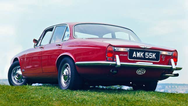 A photo of a red Jaguar XJ12 parked in a field. 
