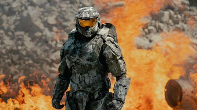 Halo protagonist Master Chief stands in front of a fiery inferno.