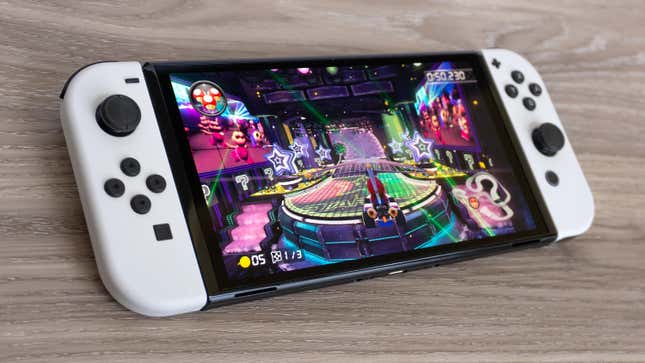 The Nintendo Switch OLED showing a game of Mario Kart on top of a wood table.