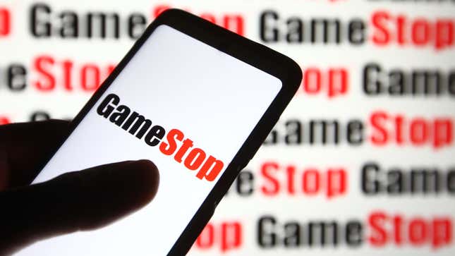 A cellphone with "GameStop" on the screen, held in front of a GameStop background.