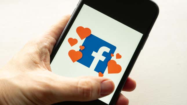 A person holding a phone with the Facebook logo surrounded by hearts
