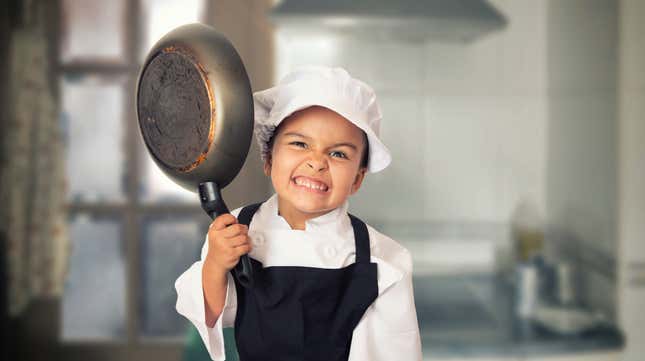 Little girl in chef's uniform holding up skillet