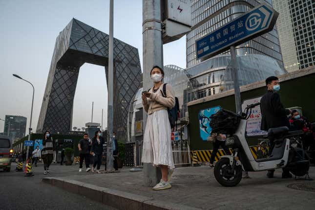 A woman looks at her mobile phone as she waits for a bus during evening rush hour in Beijing's central business district