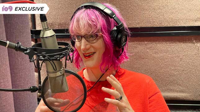 Author Charlie Jane Anders is seen recording the audiobook for her latest release, Never Say You Can't Survive. She's wearing a bright orange t-shirt and has neon pink hair.