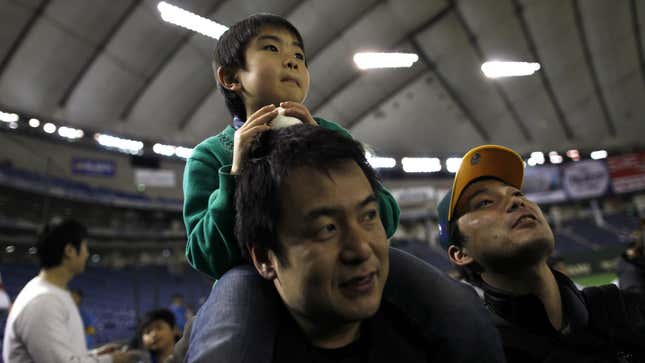 father japan paternity leave parenting parental leave abe shinzo Sota Miki, 6, sitting on his father Yoshihiko's shoulders watch players after a baseball exhibition game between Oakland Athletics and Yomiuri Giants in Tokyo March 25, 2012. REUTERS/Toru Hanai