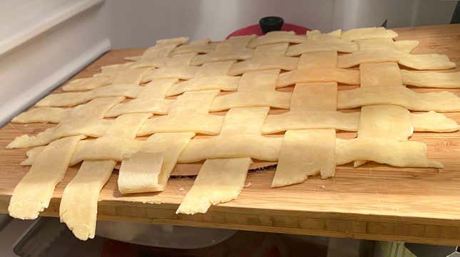 Lattice pie crust on a cardboard circle and cutting board in the fridge to chill.