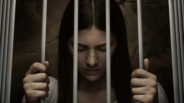 Lianne casts down her eyes while holding onto the bars of the cradle she's trapped inn.