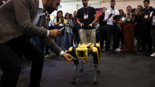 A human stretches his hand out to a robot at a demonstration as a crowd looks on.