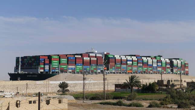 A picture taken on March 29, 2021 shows the Panama-flagged MV ‘Ever Given’ container ship (background) after being fully dislodged from the banks of the Suez Canal, near Suez city. - The vessel, a megaship the length of four football fields, was refloated and the Suez Canal reopened to traffic in the afternoon, sparking relief almost a week after the huge container ship got stuck and blocked a major artery for global trade. 