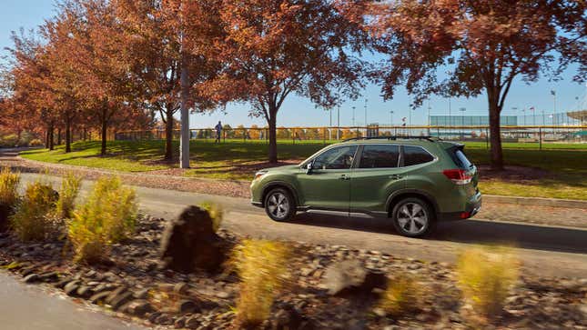 A photo of a green Subaru Forester SUV driving down a tree-lined street. 