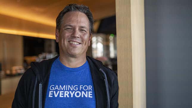 Phil Spencer grins while wearing a blue t-shirt that says "Gaming for Everyone."