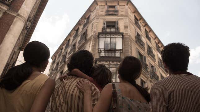 A family, photographed from the back, stares up at the windows of their apartment building.