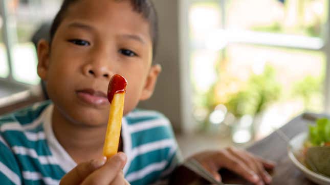 Boy eating French fry with ketchup.