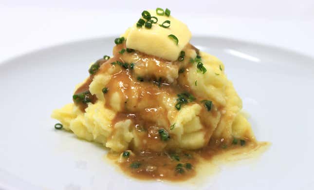 Pile of mashed potatoes on white plate with gravy, chives, and butter