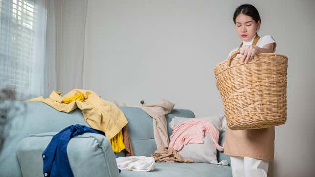 Woman holding a basket, clothes strewn on a couch