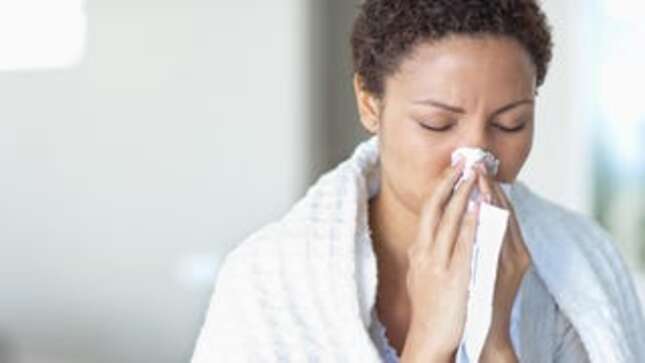 A woman with a white blanket over her shoulders blows her nose.