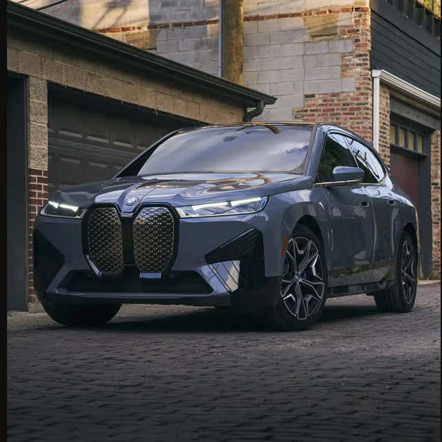 A gray BMW iX electric SUV is parked in front of a garage.