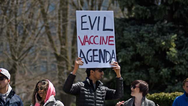 A protestor holds up a sign reading "EVIL VACCINE AGENDA" in a crowd
