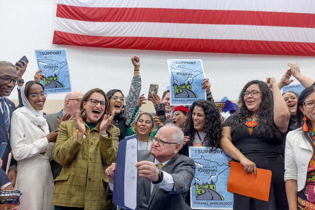Supporters, politicians and bill authors react after Minnesota Gov. Tim Walz, center, signed the &quot;Driver&#39;s Licenses for All&quot; bill at the Cedar Street Armory, March 7, 2023, in St. Paul, Minn. People living in Minnesota without legal immigration status can now begin the process of getting their driver&#39;s license by making an appointment for their written driver&#39;s test, state officials announced at a news conference Thursday, Sept. 7. (Elizabeth Flores/Star Tribune via AP)