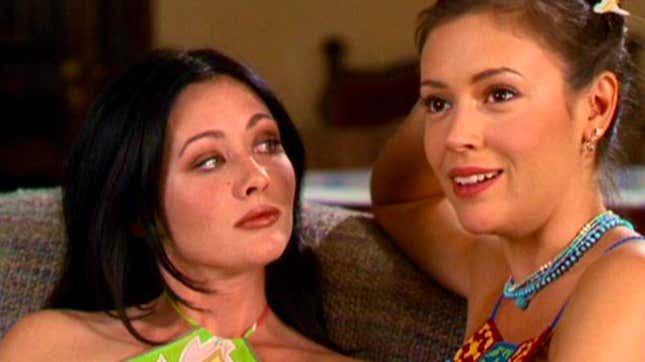 Prue Halliwell (Shannen Doherty), bored and sitting on a couch as she listens to her younger sister, Phoebe (Alyssa Milano), who is sitting next to her, prattle on.
