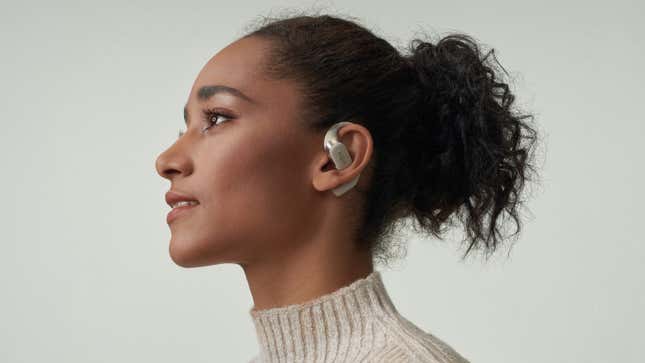A person wearing the beige version of the Shokz OpenFit wireless earbuds against a neutral background.