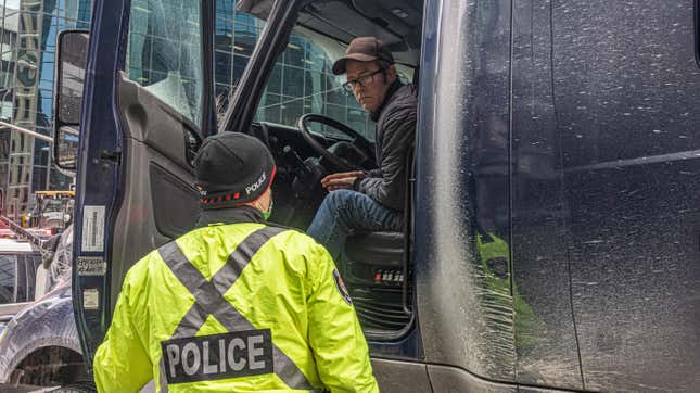 OTTAWA, ON - JANUARY 31: A police officer speaks with a trucker blocking the street on January 31, 2022 in Ottawa, Canada. Thousands turned up over the weekend to rally in support of truckers using their vehicles to block access to Parliament Hill, most of the downtown area Ottawa, and the Alberta border in hopes of pressuring the government to roll back COVID-19 public health regulations. 
