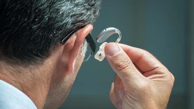 An older man viewed from the back, from the shoulders up, removing a hearing aid from his ear