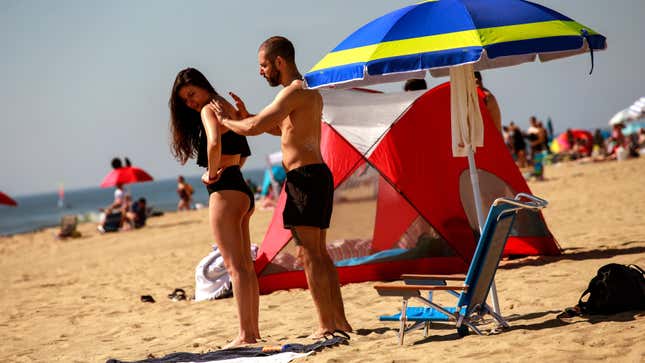 A man applies sunscreen to a woman as they visit the beach during Memorial Day weekend on May 26, 2019 in Asbury Park, New Jersey.