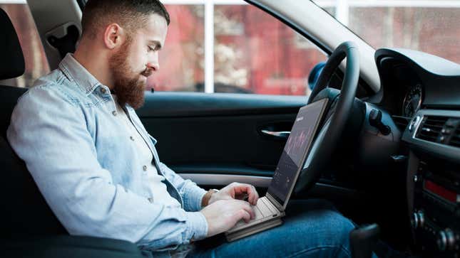 A person shown using a mockup of the Compal Electronics Mobile Office concept laptop while sitting in the driver's seat of a vehicle.