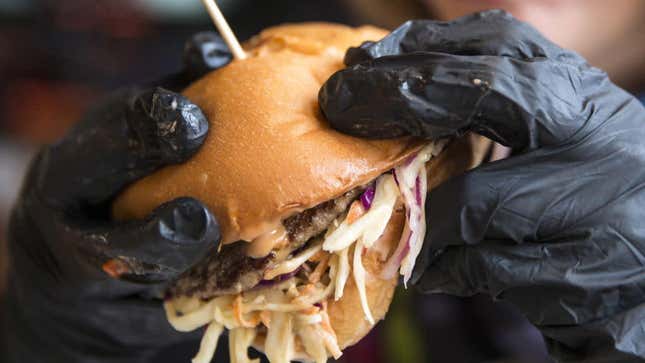 A woman in black gloves holds a hamburger in a Black Star Burger in Grozny, Chechen Republic, Russia