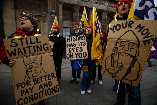 Members from the STUC, UCU, RMT and PCS unions hold signs at a protest. One sign reads "Still waiting for better pay and conditions," another "your move," and a third reads "history has its eyes on you."