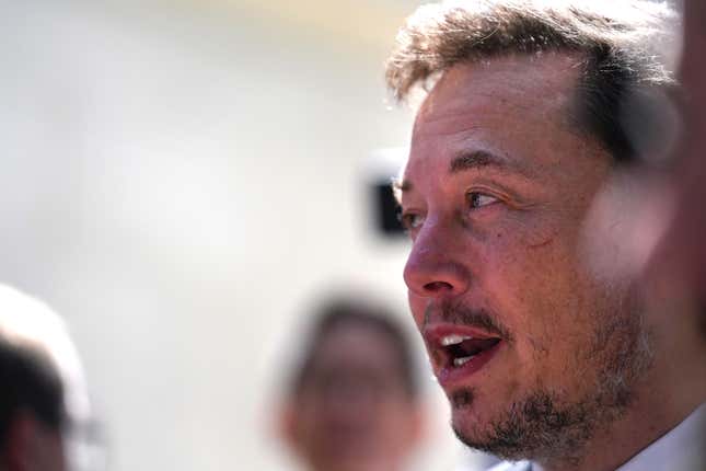 Elon Musk's looks off to the side of the screen, mouth agape. He is unshaven.