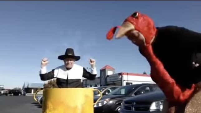A man is being deep fried while a turkey dances in a dealership parking lot.