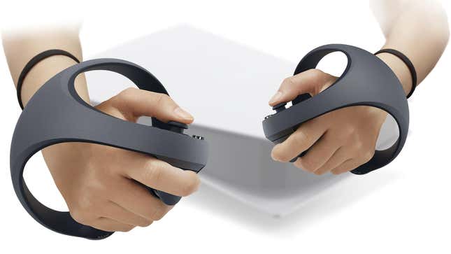 Two hands grip the upcoming controllers for Sony's PSVR2 virtual reality system. In the background a PS5 is visible.