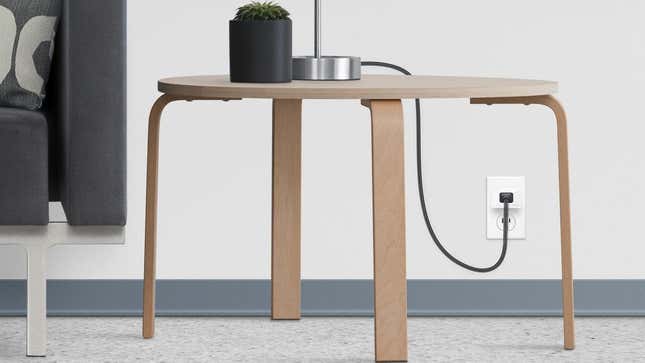 A Wemo Smart Plug With Thread connected to a lamp on a side table.
